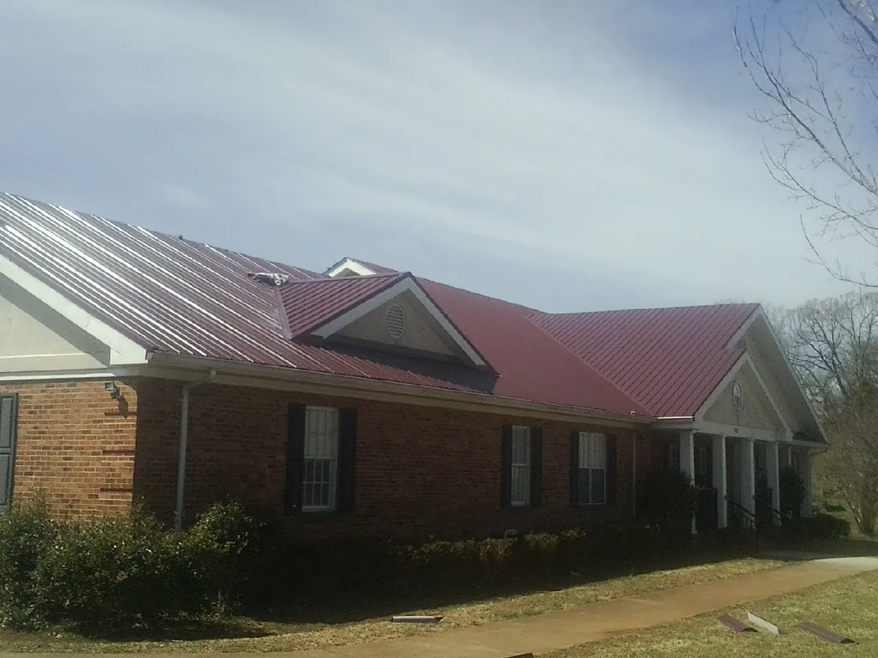 Red metal roof with gabled entries on a long brick building, from a Hail Damage Roof Repair job in Ione