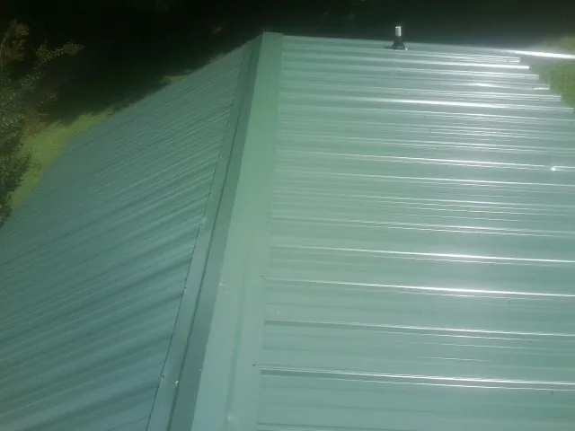 New green metal panels meeting at the ridge of a roof — Flat Roof Repair work by our crew in Ione