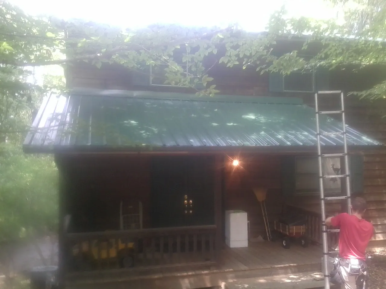 Worker on a ladder at the green porch roof of a wooded cabin in Ione