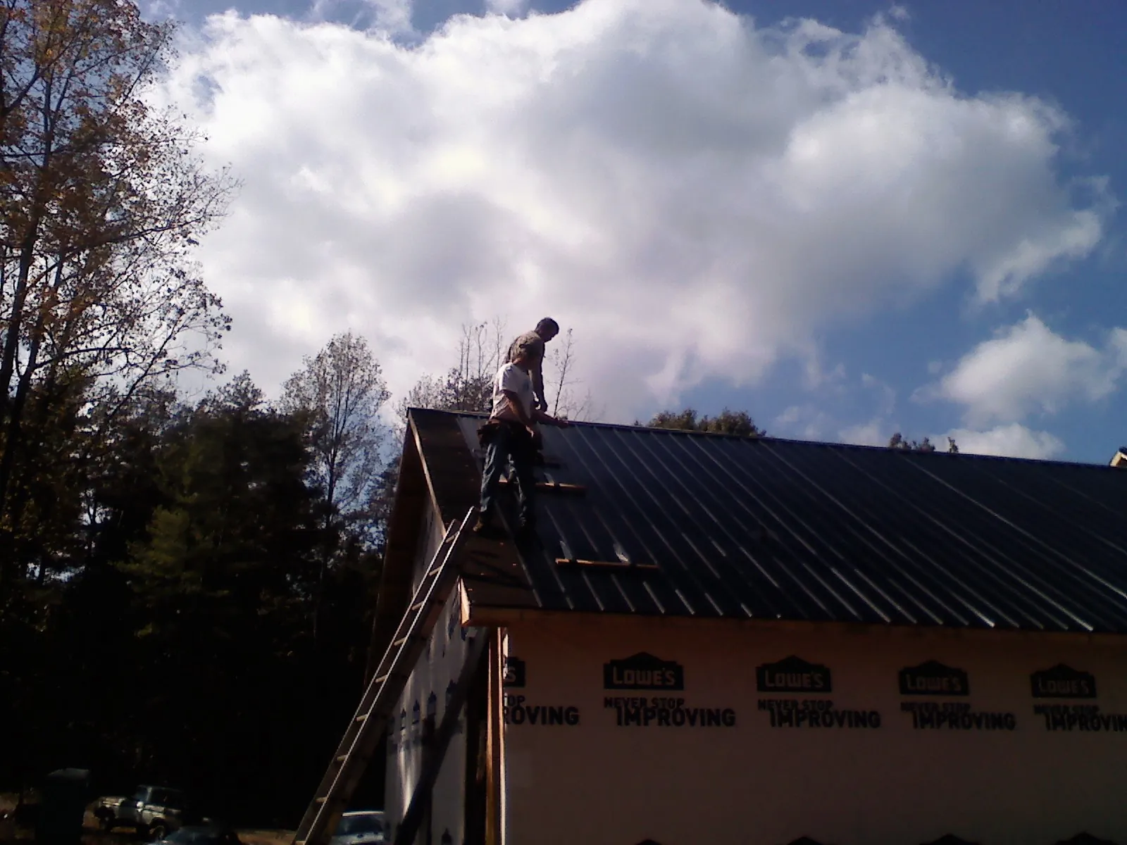Roofer fastening dark metal panels high against a cloudy sky, from a Roof Inspection job in Ione